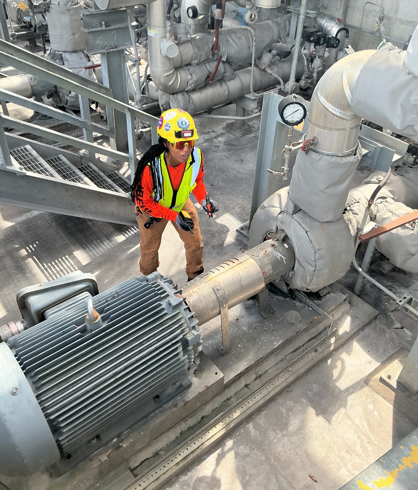 ELEKproTEK electrician inspecting a large electric motor and insulated process pump on an industrial plant platform
