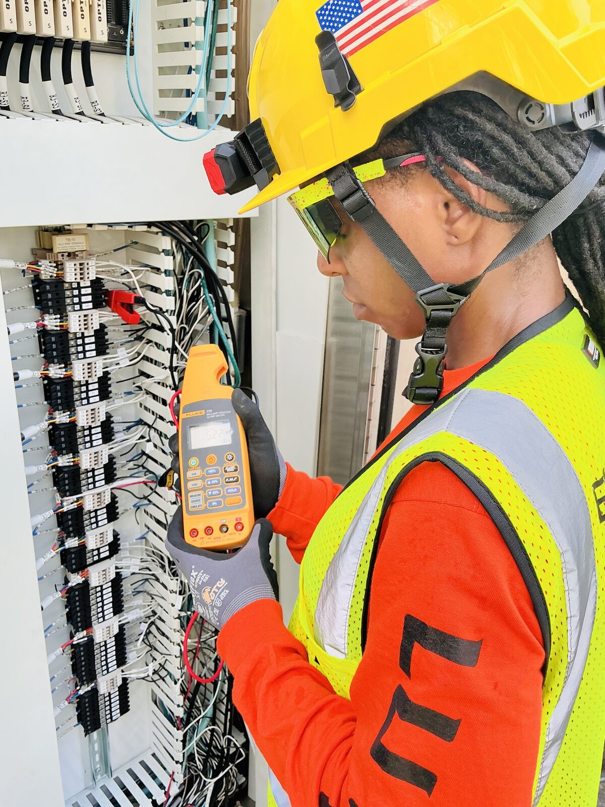 Electrician reading a Fluke 773 milliamp process clamp meter beside a wired control panel with Opto 22 modules