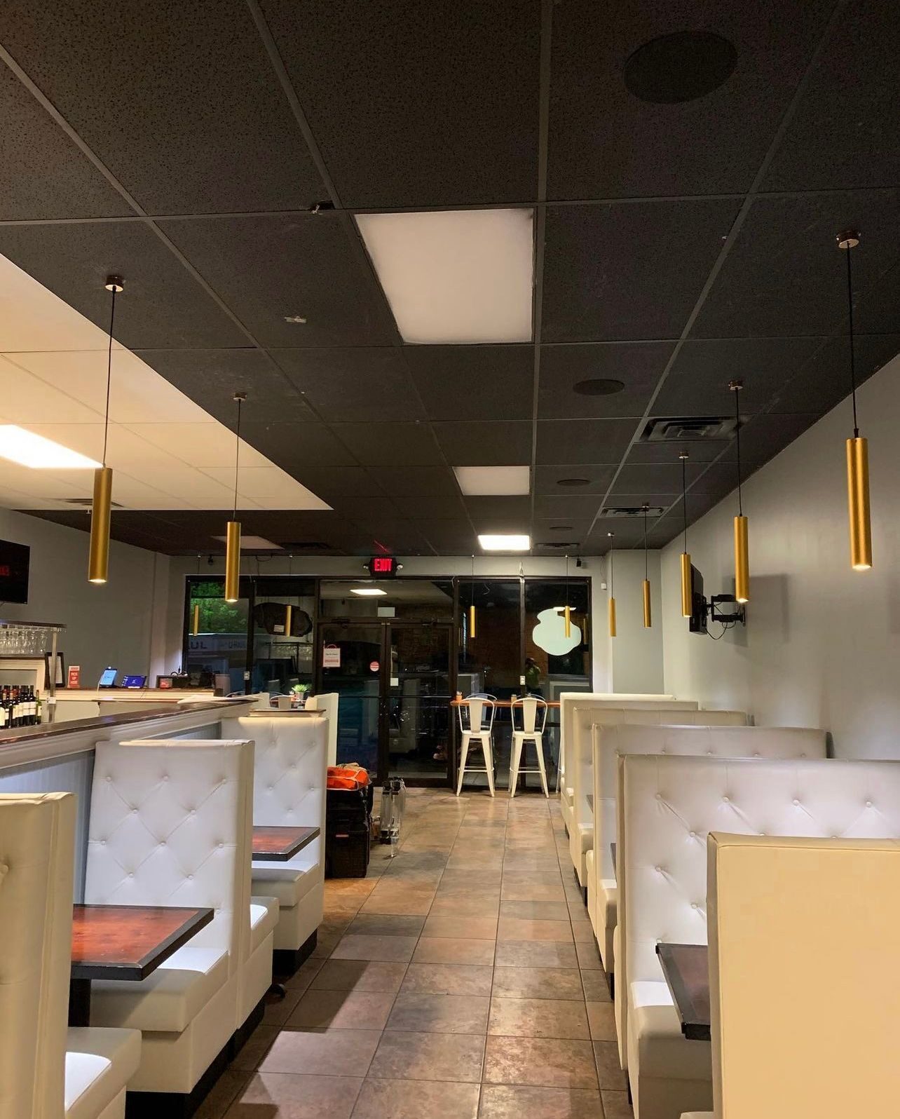Restaurant dining room with white booth seating, gold pendant lights, and recessed ceiling fixtures