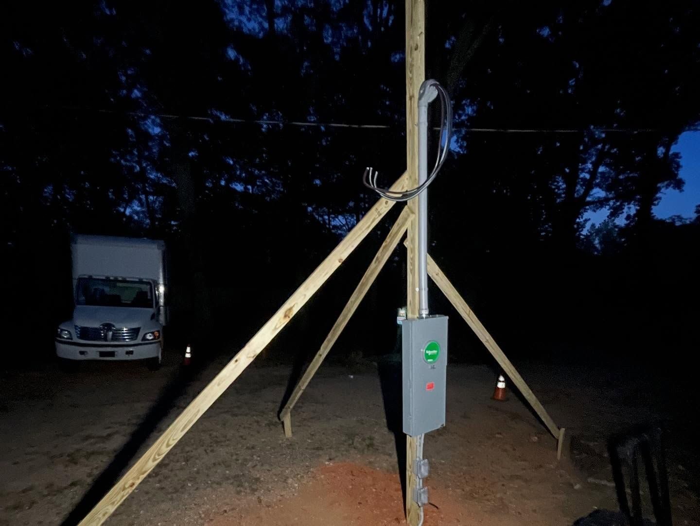 Wooden temporary power pole braced with timber stakes and a mounted disconnect box at dusk