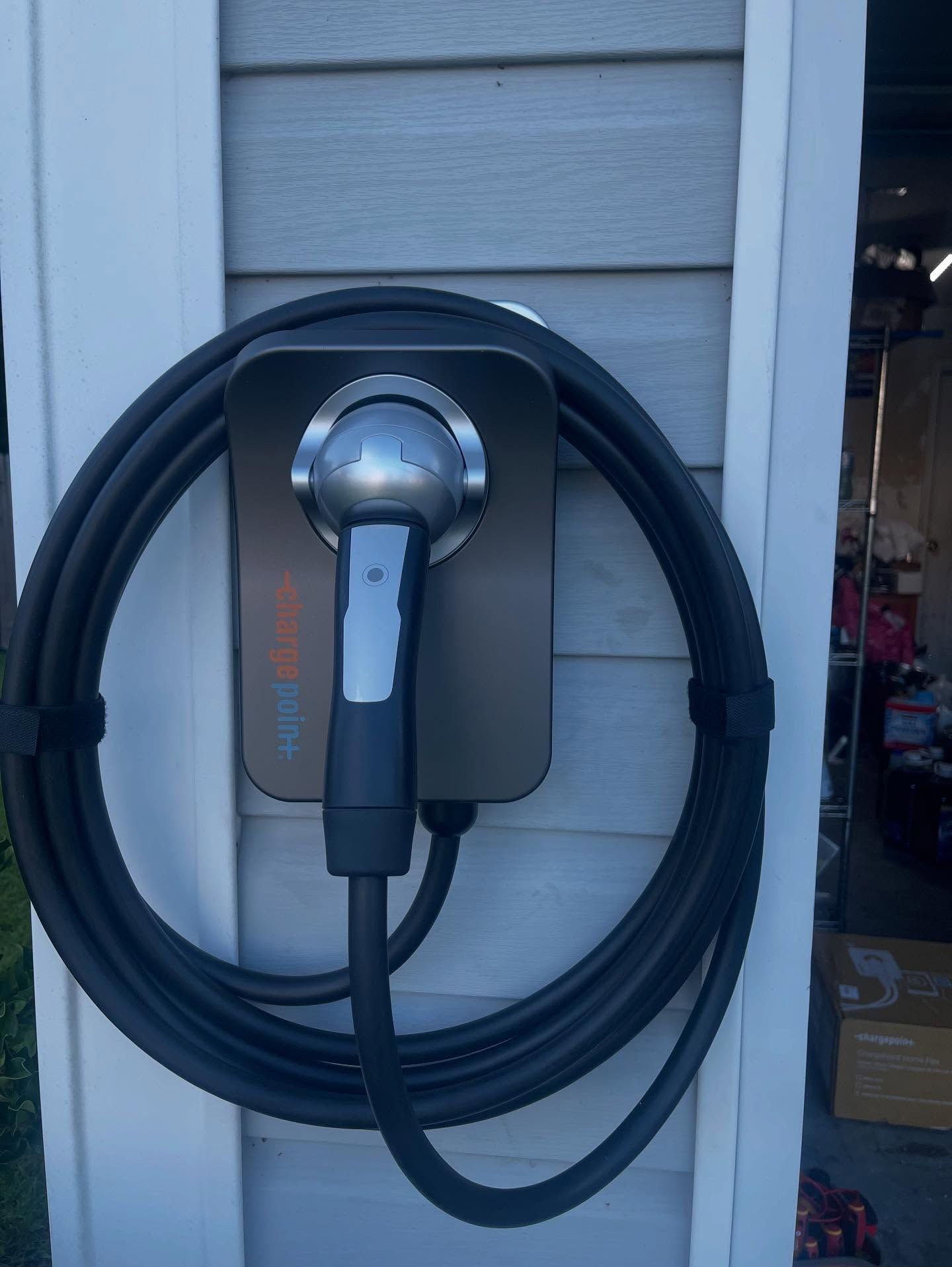 Wall-mounted EV charger with its black cable coiled around the holder on a siding wall.