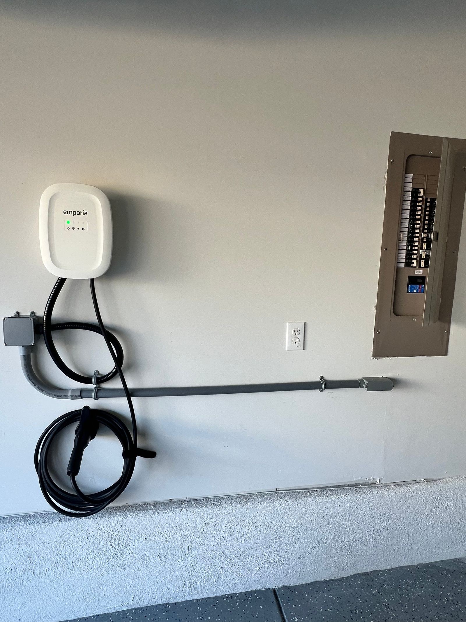 White wall-mounted EV charger beside a panel with a conduit run along the wall.