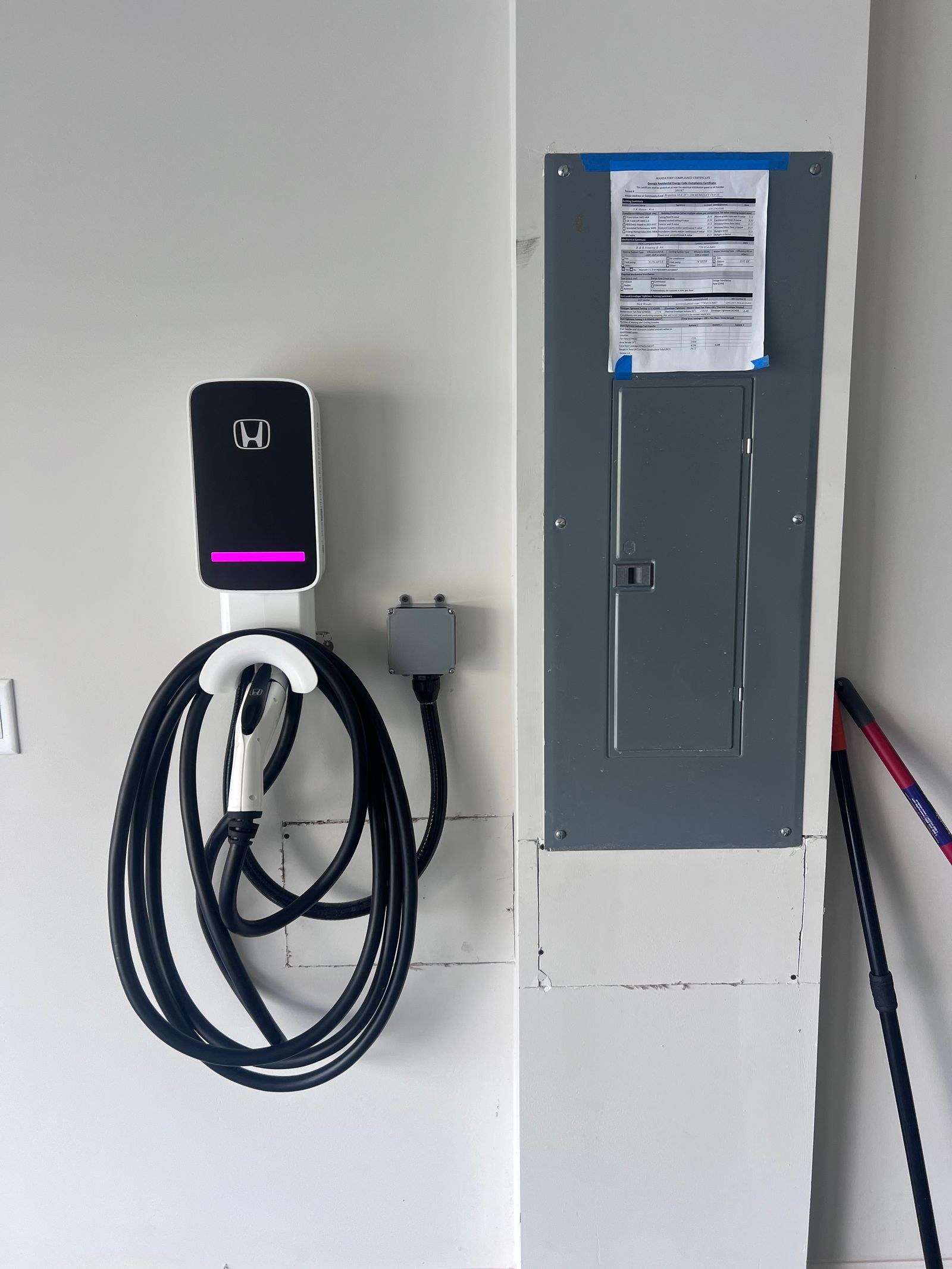 White wall charger with a pink status light mounted beside a gray electrical panel.