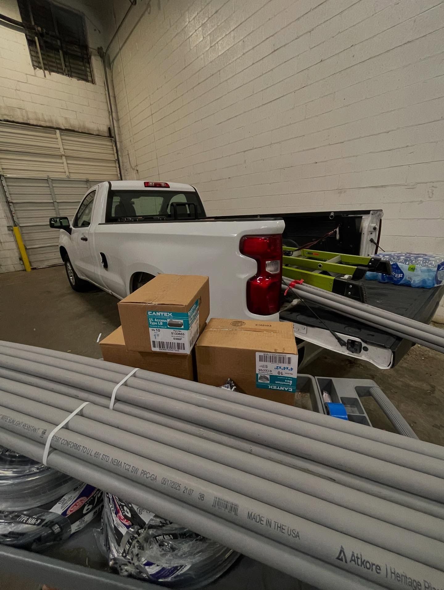 Bundles of gray PVC conduit and boxes of fittings loaded in the bed of a white work truck inside a warehouse.