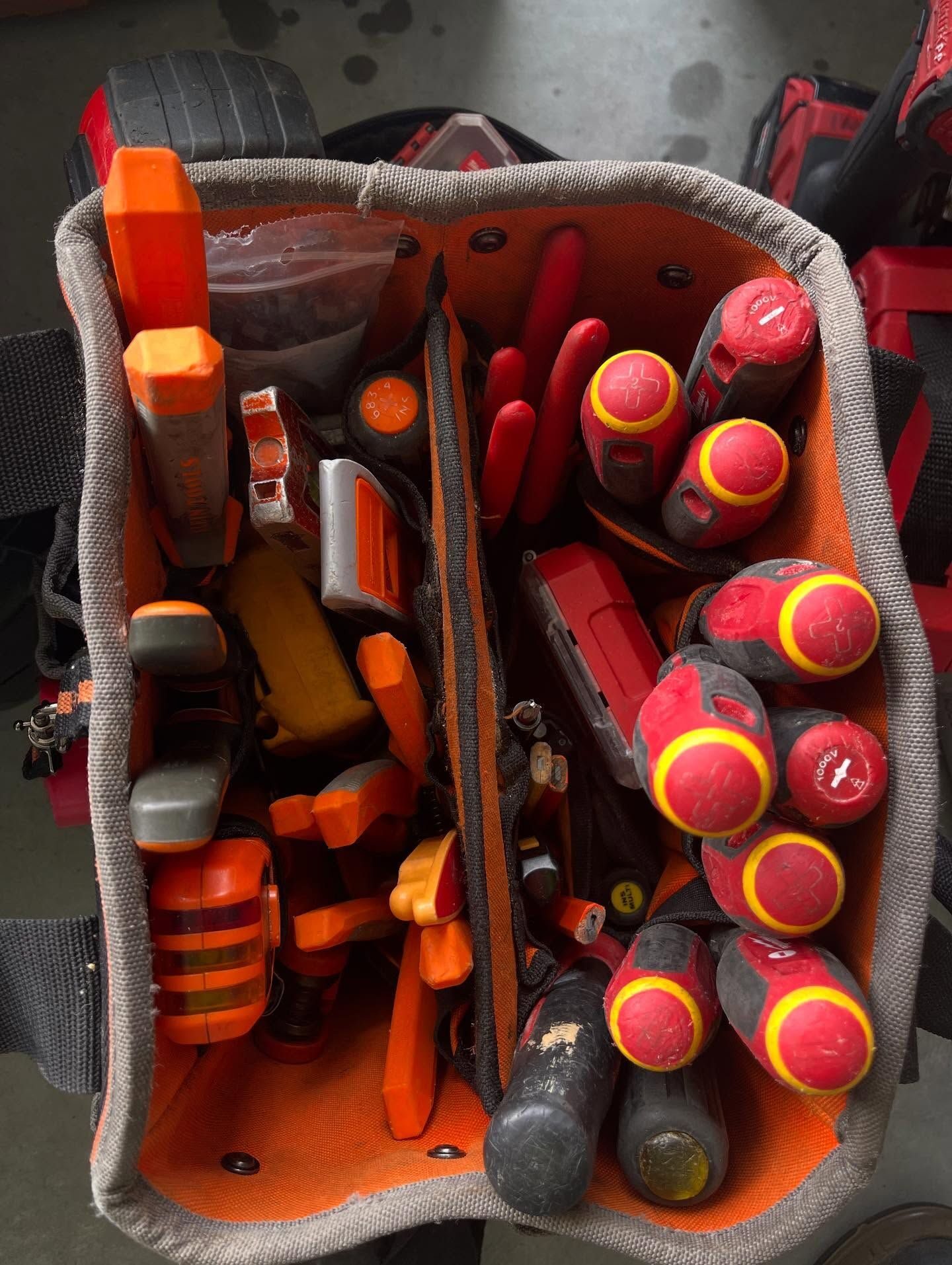 Top-down view of an orange tool bag packed with insulated screwdrivers and pliers.