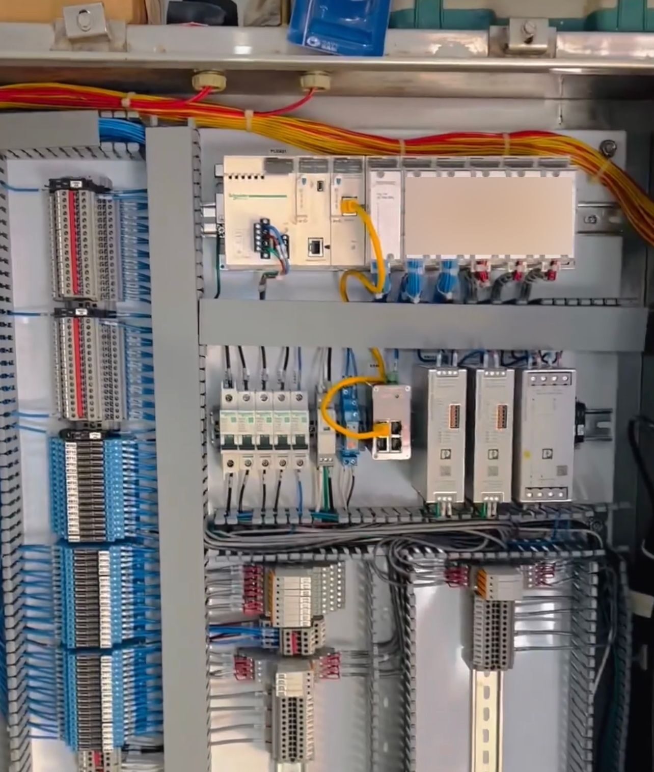 Control panel with a PLC rack, power supplies, small breakers, and columns of blue-wired terminal blocks.