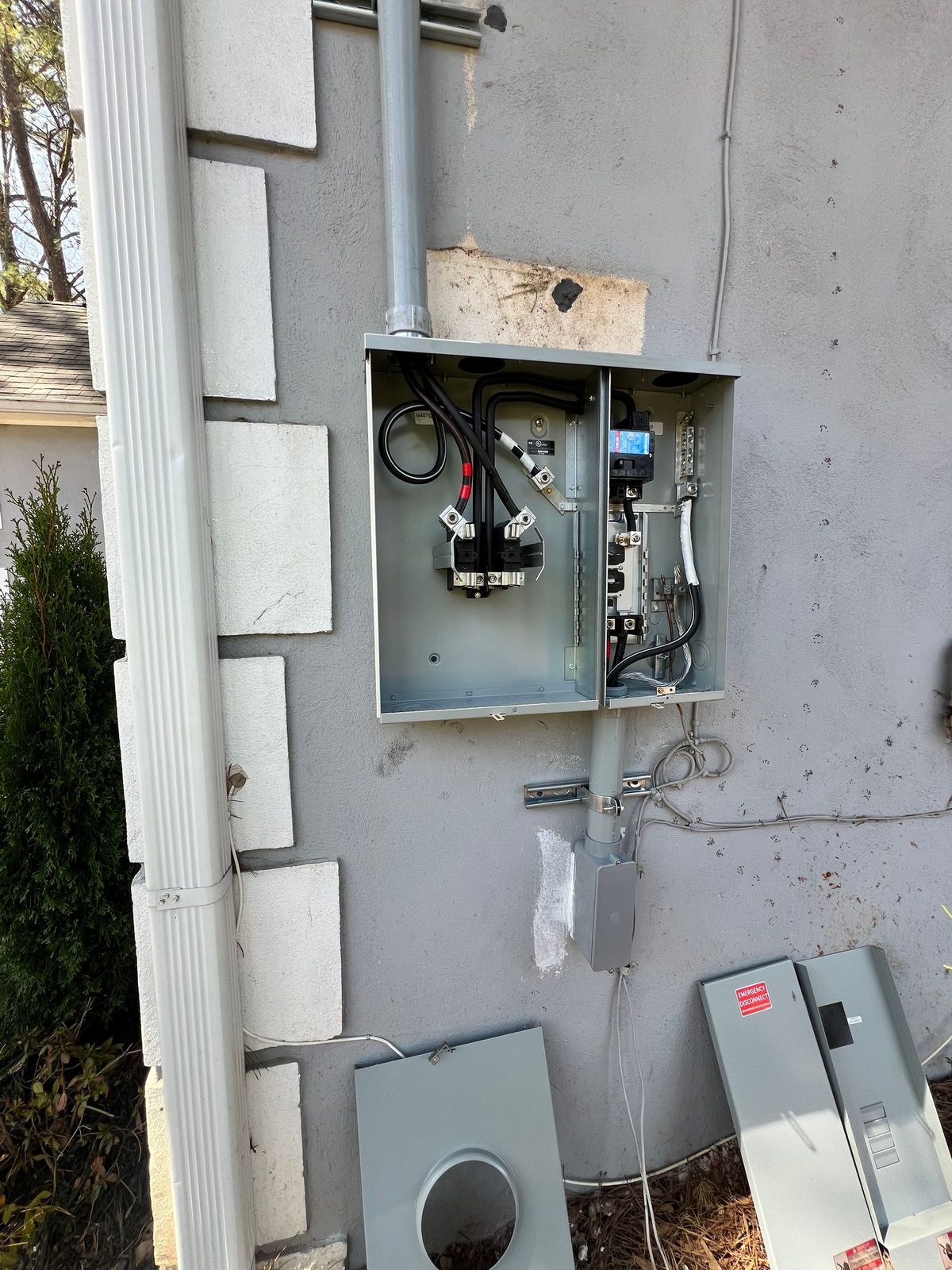 Exterior meter enclosure opened on a stucco wall with disconnect pieces on the ground below