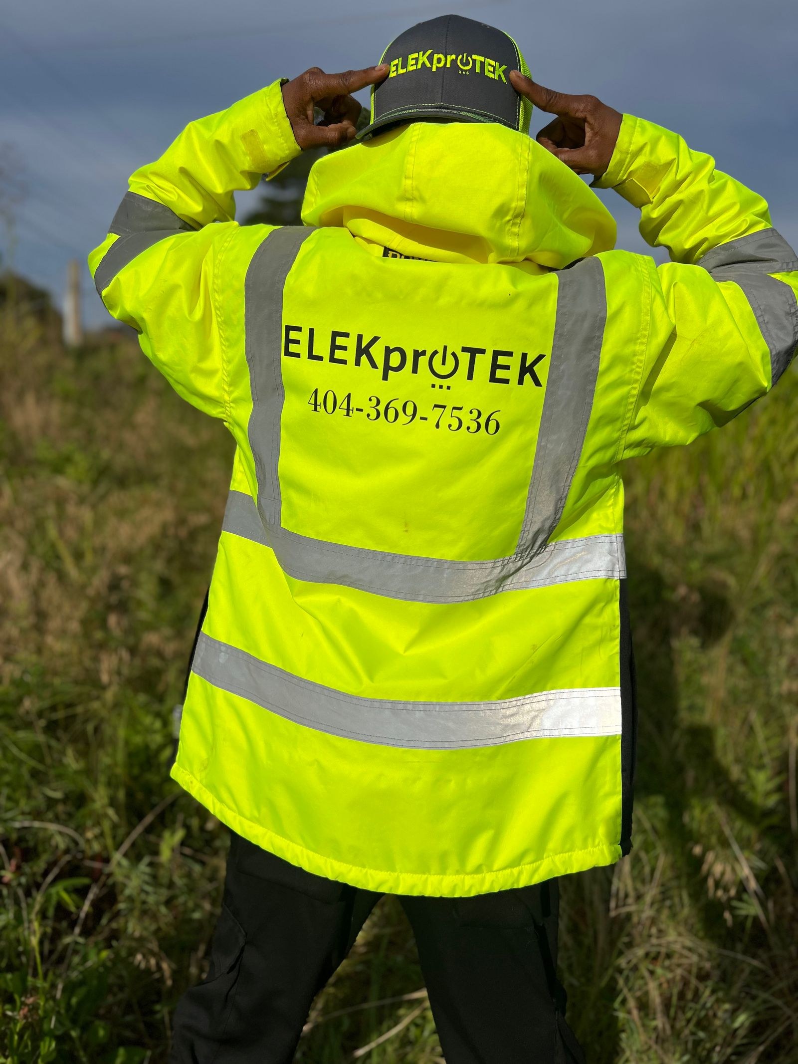 Technician in a hi-vis jacket and cap standing in a grassy field, seen from behind.