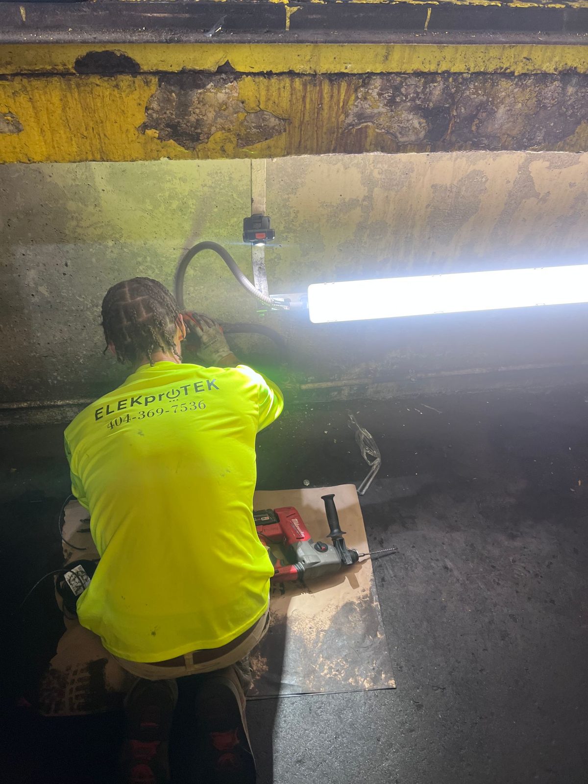 Technician kneeling in a concrete loading dock bay beside a bright LED strip light with tools laid out on a board