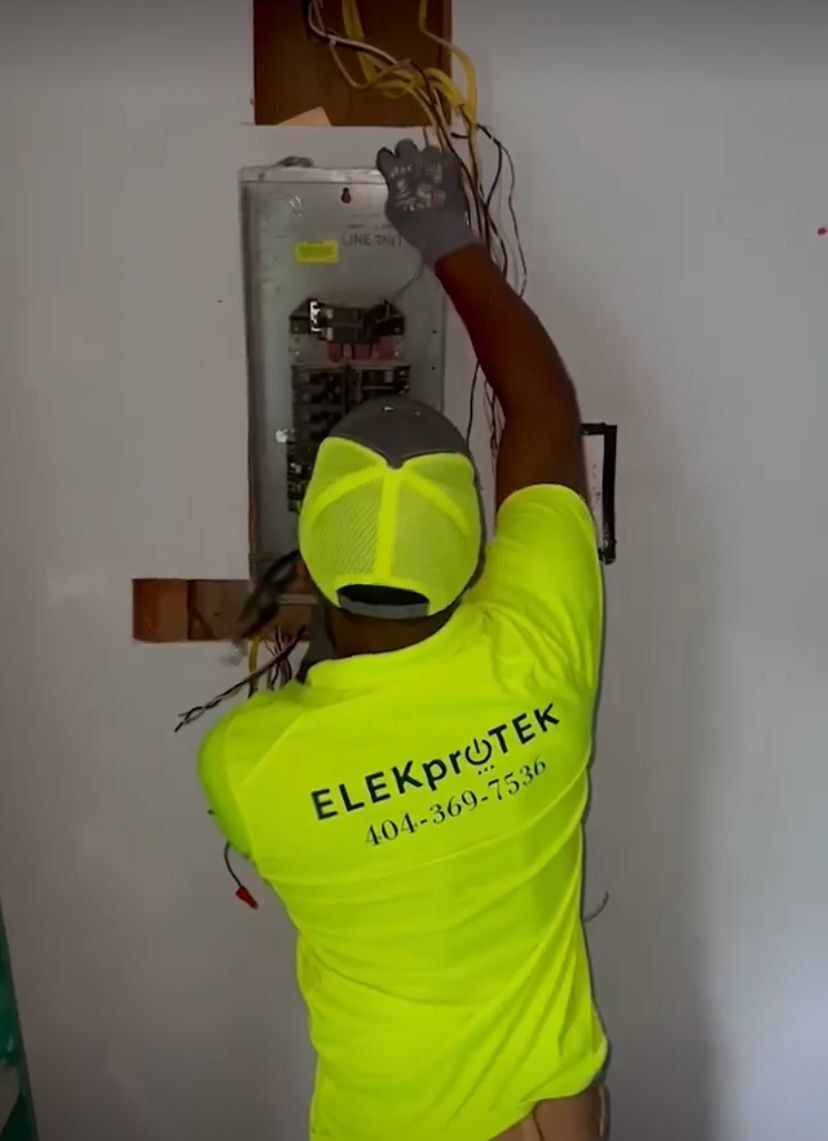 Technician in a lime cap reaching into an older wall-mounted panel with cables hanging from the top.