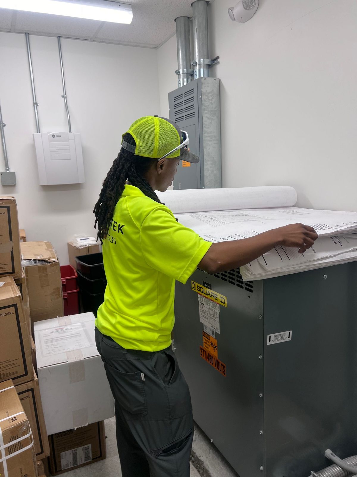 Technician in a cap and safety glasses unrolling drawings on top of a dry-type transformer in an electrical room